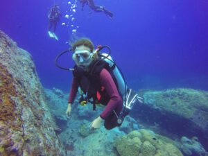 A scuba diver explores a vibrant underwater scene with rocky coral formations and colorful marine life in a deep blue ocean.