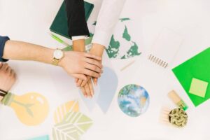 Four hands stacked together on a table, surrounded by eco-themed illustrations and notebooks