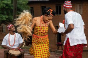 A woman in traditional attire dances energetically, while a drummer provides rhythm, showcasing vibrant cultural celebration.