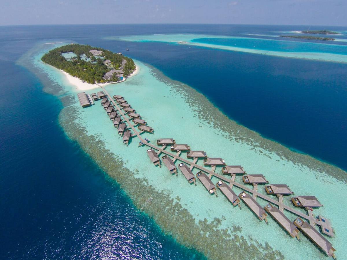 Aerial view of a luxurious island resort featuring overwater bungalows, turquoise waters, and lush greenery. Perfect tropical paradise.