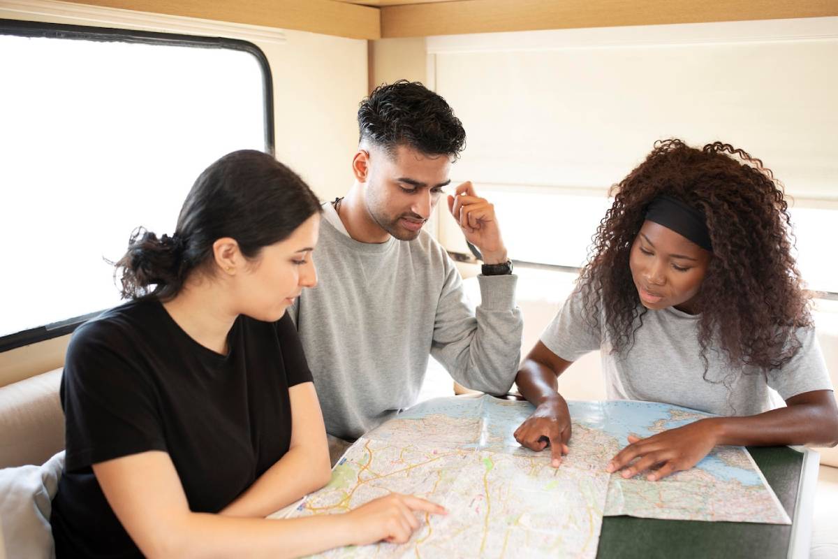 Three people studying a map on a table inside a cozy RV, engaged in conversation and planning their route together. 