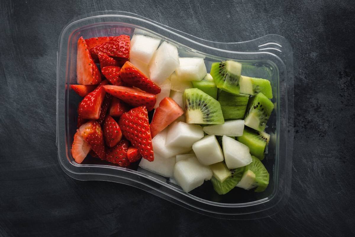 A clear container filled with fresh strawberries, honeydew melon, and green kiwi pieces arranged neatly. 