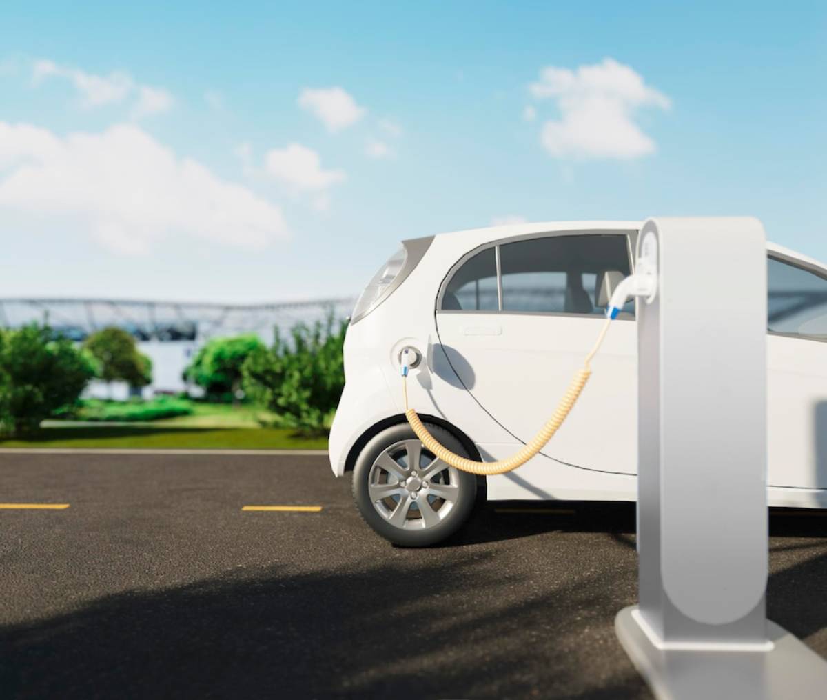 A white electric car is parked and charging at a station on a sunny day, surrounded by greenery and a clear blue sky. 