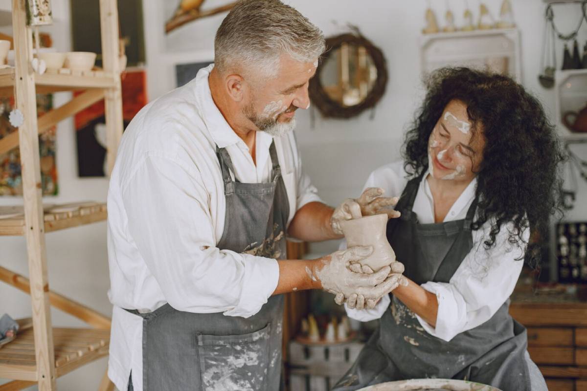Two artists are collaboratively shaping clay pottery, surrounded by tools and a creative studio atmosphere. 