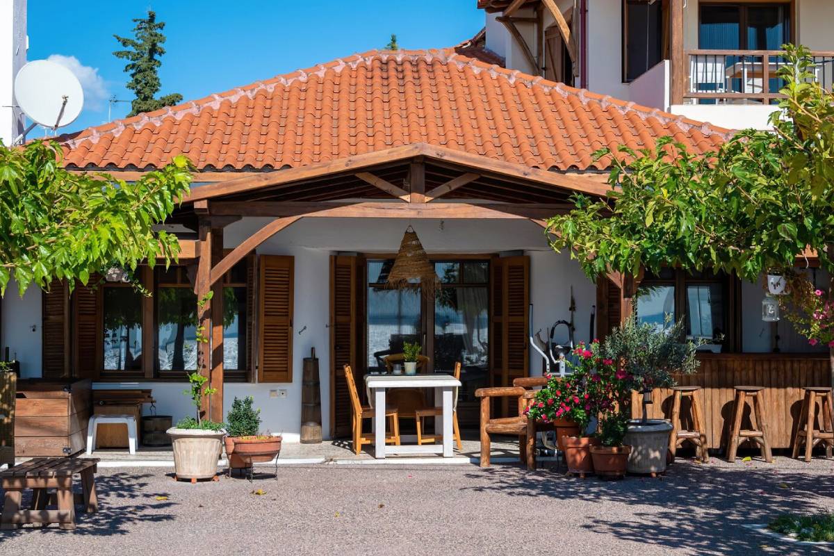 Charming house with a terracotta roof, wooden porch, potted plants, and outdoor seating under a bright blue sky. 