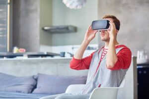 A young man wearing a virtual reality headset sits in a modern living room, engaged in an immersive experience.