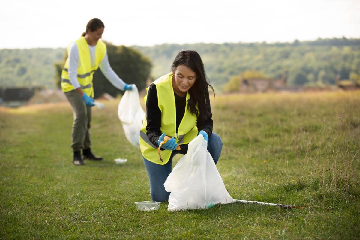  Two individuals in yellow vests collect litter in a grassy field, promoting environmental cleanliness and community service.